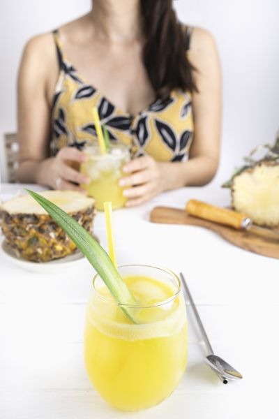 Refreshing homemade pineapple juice with ice. Girl at a table drinking a pineapple juice. Cool drink for summer. Healthy drink with vitamins