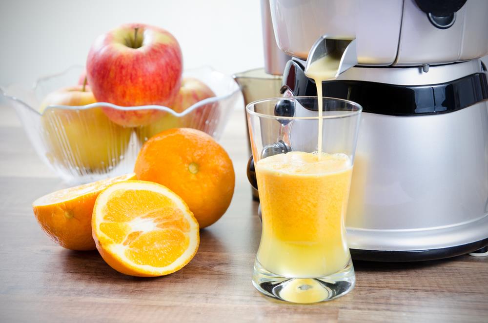 A juicer producing juice, with apples and oranges on the side