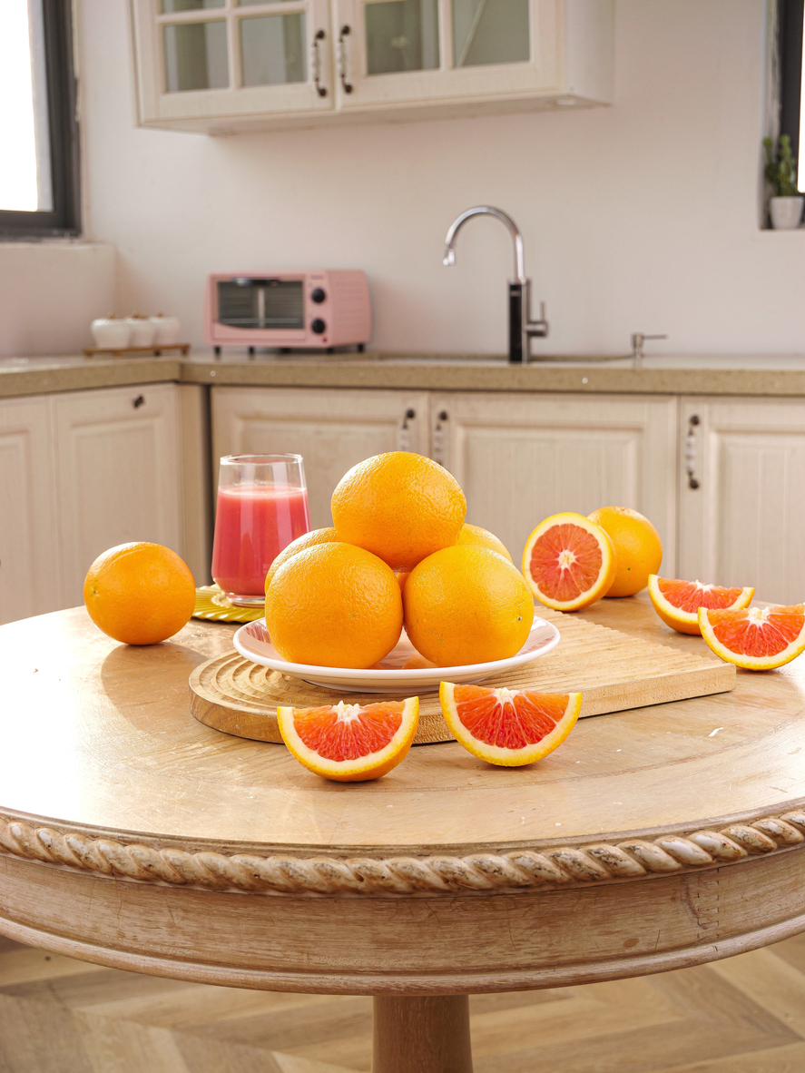 Fresh blood oranges and grapefruit slices arranged on wooden plate in bright modern kitchen with red juice glass