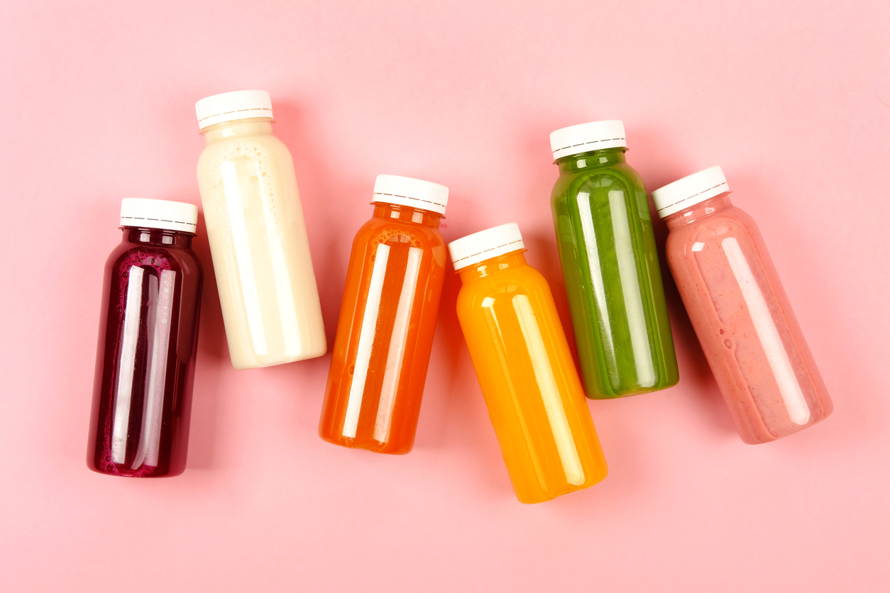 Bottles of multicolored smoothies or juices on pink background