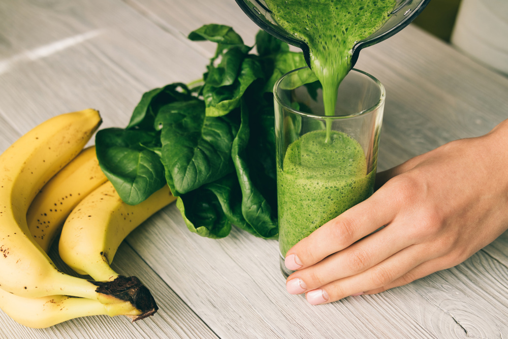 Female hand pours a smoothie of banana and spinach in glass on a wooden table