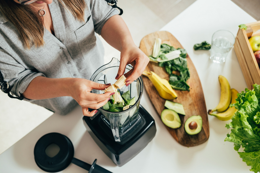 Woman is preparing a healthy detox drink in a blender - a green smoothie with fresh fruits, green spinach and avocado
