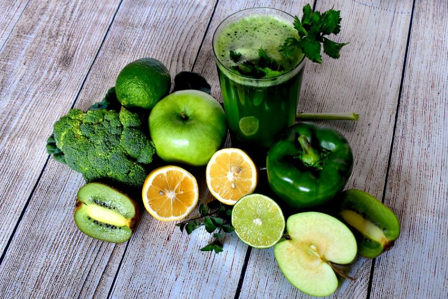 a glass of green juice surrounded by green fruits and vegetables