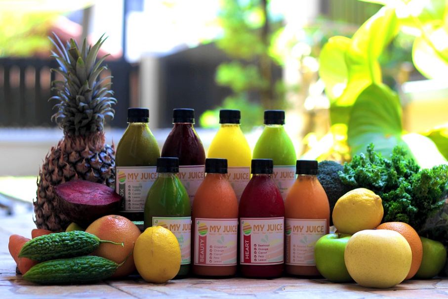 bottles of colorful juice surrounded by fruits and vegetables