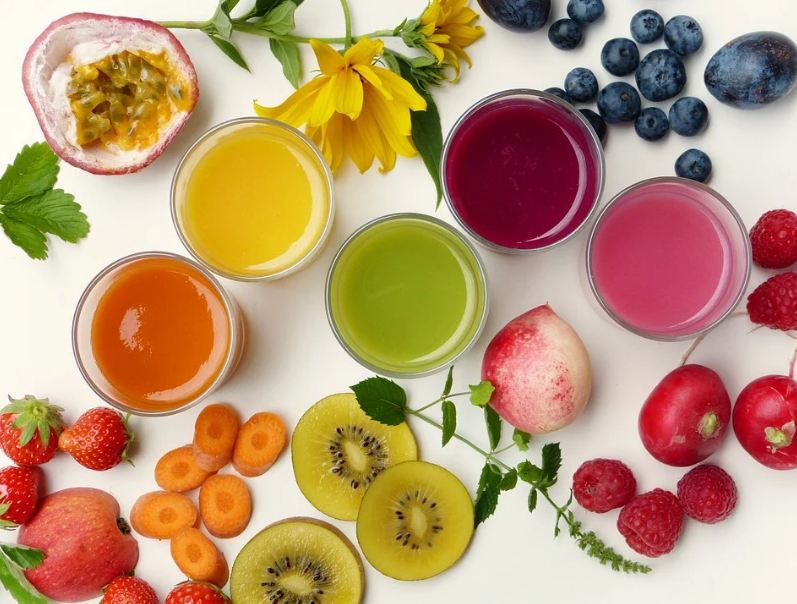 glasses of colorful juices surrounded by fruits, vegetables, herbs and flowers
